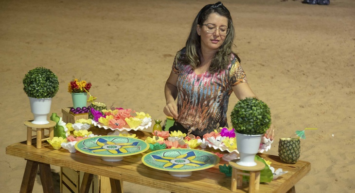 A técnica de enfermagem Silvia Patrícia prepara a mesa de docinhos para receber convidados nas areias da praia