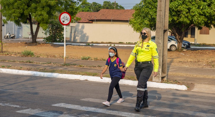 Agente de trânsito conduz aluna durante travessia da faixa de pedestre