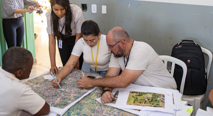 Mary Dias (em pé próxima ao mapa), coordenadora de Projetos Sociais ajuda morador a encontrar no mapa urbanístico seu novo endereço