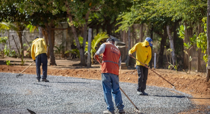Trabalhadores espalham brita para dar acabamento a pavimento feito de tratamento superficial duplo (TSD)