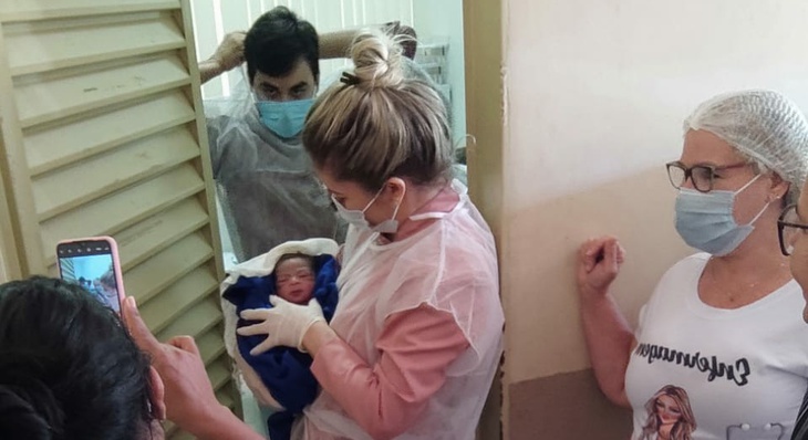 Ao fundo, médico Nikolas observa enfermeira Vânia segurando bebê homônimo