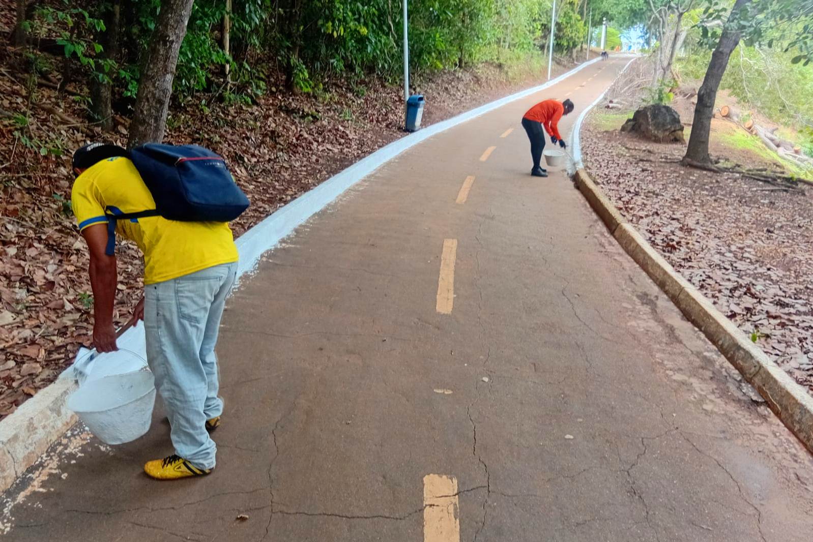 Trabalhadores realizam a pintura de meio-fio da pista de caminhada, delimitando a área de segurança